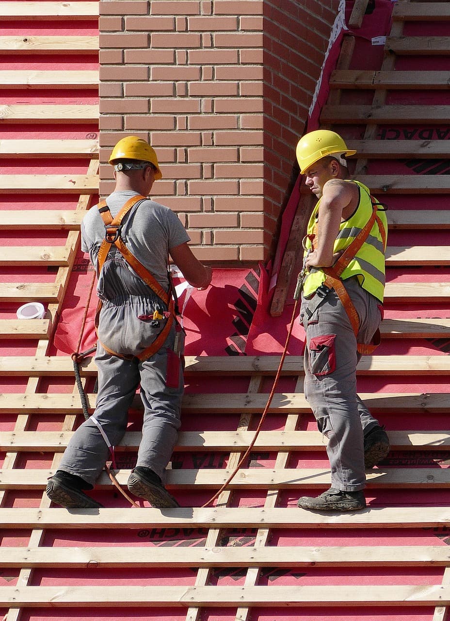 Two roofers in hard hats and harnesses installing roof battens